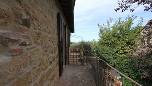 A narrow stone pathway leading to a wooden door, surrounded by greenery and a metal railing.