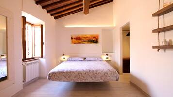 A bedroom with a bed, bedside lamps, a painting on the wall, and a wooden ceiling.