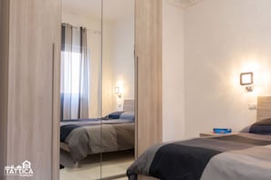 A hotel room with a large mirror, a bed, a bedside table, and a nightstand.