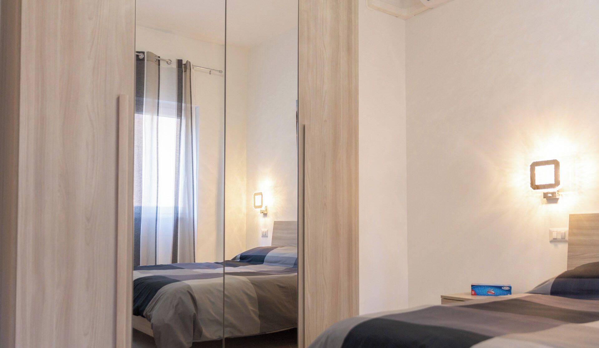 A hotel room with a large mirror, a bed, a bedside table, and a nightstand.