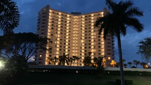 Ein mehrstöckiges Hotel mit geschwungener Fassade, beleuchteten Fenstern und von Palmen umgeben.