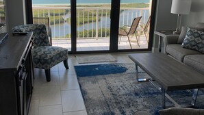 Ein modernes Wohnzimmer mit einem großen Schiebeglasfenster, das auf einen Balkon mit Meerblick führt.