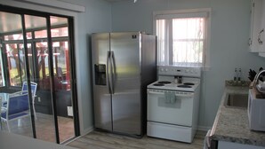 A kitchen with a stainless steel refrigerator, a white stove, and a window with blinds.