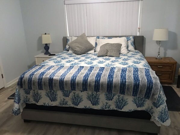 Una cama con una colcha azul y blanca estampada, dos lámparas de noche y una mesita de noche con lámpara.