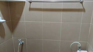 Un baño pequeño con inodoro, un cubo azul y una manguera.