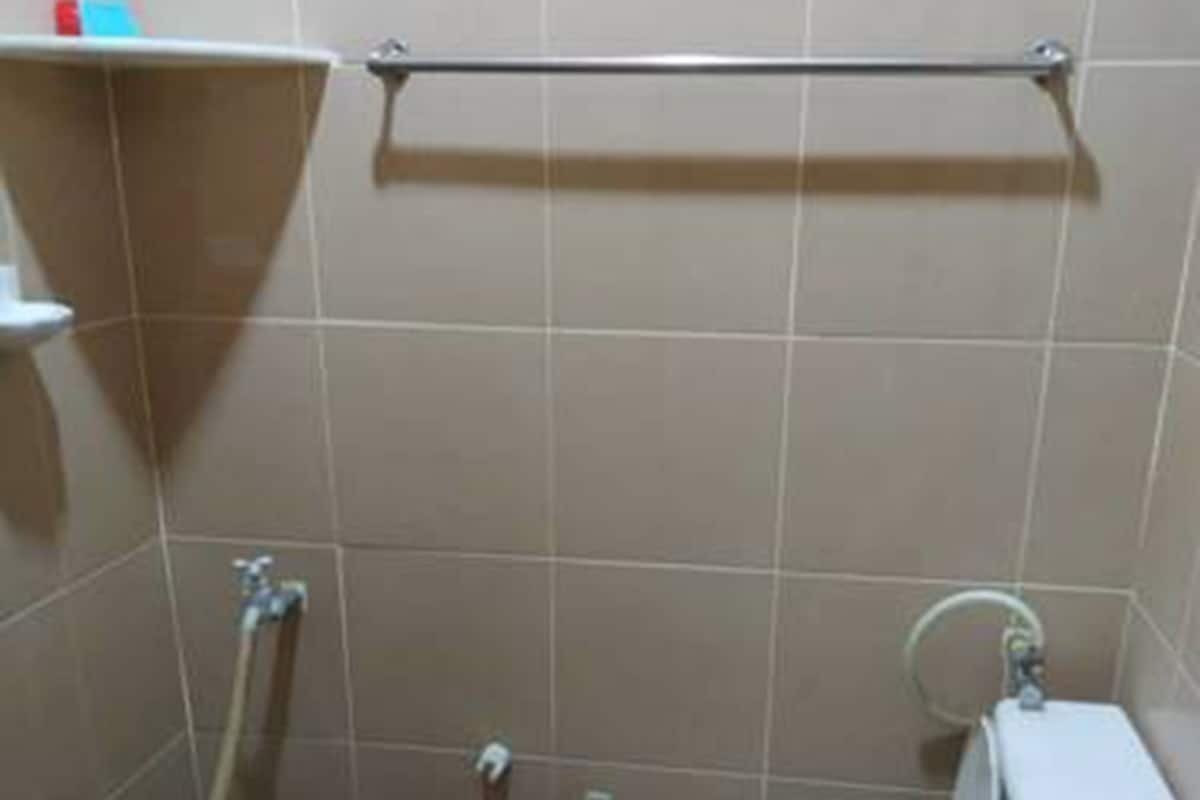A small bathroom with a toilet, a blue bucket, and a hose.