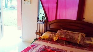 Un dormitorio con cama, una ventana con cortinas, una mesita de noche y una silla.