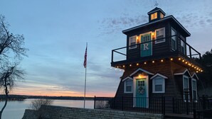 A two-story wooden building with a turquoise door and a flagpole with an American flag. - Lakefront property with pool and lighthouse with amazing views of the lake, . (Granbury)