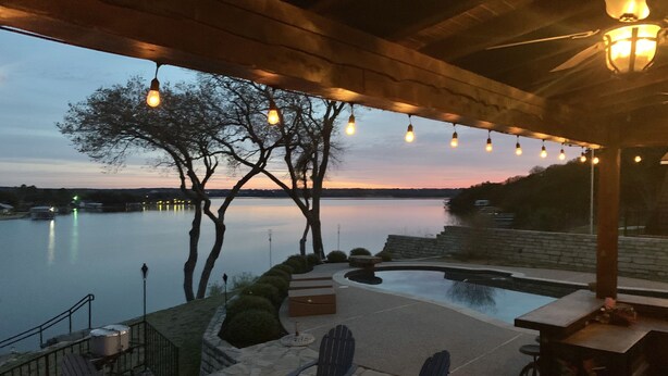 An outdoor patio with a stone fire pit, Adirondack chairs, and a view of a calm lake at dusk. - Lakefront property with pool and lighthouse with amazing views of the lake, . (Granbury)
