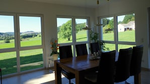 A dining area with a large table and chairs, large windows with a view of a green landscape. - Holiday house with large garden and wonderful view (Weinsfeld)