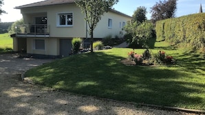 A two-story house with a balcony, a driveway, and a well-maintained lawn with flowers. - Holiday house with large garden and wonderful view (Weinsfeld)