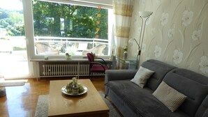A living room with a grey sofa, a wooden coffee table, and a view of greenery outside. - Holiday house with large garden and wonderful view (Weinsfeld)