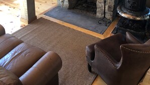 A stone fireplace with a mantel shelf, a black stove, and a brown leather armchair. - 10+ Spacious Cape on Winnipesaukee Island. Private Peninsula. Sunset Views. (Meredith)