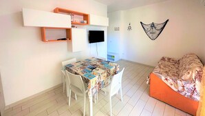 Ein kompakter Raum mit Esstisch, Stühlen, einem Bett, einem Fernseher und Einbauschränken.