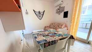 Ein Essbereich mit einem Tisch, bedeckt mit einer Patchwork-Tischdecke, weißen Stühlen, einer Wanduhr, einer Wanddekoration und einem Schild mit der Aufschrift 'HOME'.
