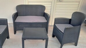 Drei Korbstühle mit Kissen und ein kleiner Tisch sind auf einer gefliesten Terrasse angeordnet.