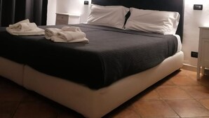 A neatly made bed with white and black bedding, a black headboard, and a white nightstand with a lamp. - B&B Il Viaggiatore (Massa)