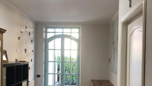 A hallway with a tiled floor, a light green door, a black shelving unit, and a patterned rug. - B&B Il Viaggiatore (Massa)