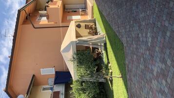 Un edificio residencial con techo plano, un pequeño jardín con césped y un sendero empedrado, y una antena parabólica en el techo.