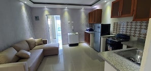 Cozy living space with a kitchenette area, featuring a sofa, door to an adjacent room, and a kitchenette with a refrigerator, stove, and sink.