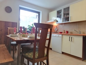 A dining area with a wooden table and chairs, a kitchen with white cabinets and a dishwasher, and a window providing natural light.