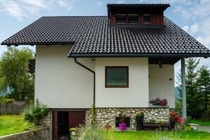 A two-story house with a stone facade, a tiled roof, and a small porch with potted plants.