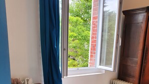 A room with a wooden desk, a radiator, a bench, and a window with a view of greenery. - Apartment 2 Ch near the beach and downtown Houlgate. (Houlgate)
