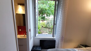 A bedroom with a bed, a window with a view of greenery, a small bedside table, and a red cabinet. - Apartment 2 Ch near the beach and downtown Houlgate. (Houlgate)