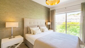 A modern hotel room with a large bed, two bedside tables, and a view of greenery through the window. - VERASL T - Albufeira - New, Luxury & comfy 2 bedrooms apartment (Albufeira)