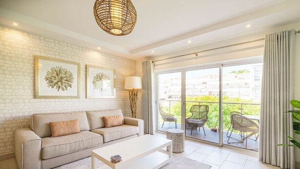 A modern living room with a sofa, coffee table, and a large window with a view of greenery. - VERASL T - Albufeira - New, Luxury & comfy 2 bedrooms apartment (Albufeira)