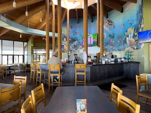 A restaurant with a high ceiling, wooden beams, and a mural of underwater scenery. - Seas The Day Leeward-Windward 607W-Beachfront Panoramic Views! Free Beach Service Included! (Panama City Beach)