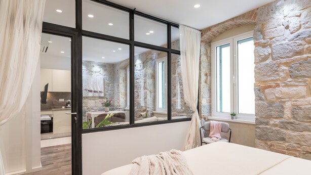 Ein Schlafzimmer mit Steinsandsteinwand, großem Fenster und Blick auf die Küche.