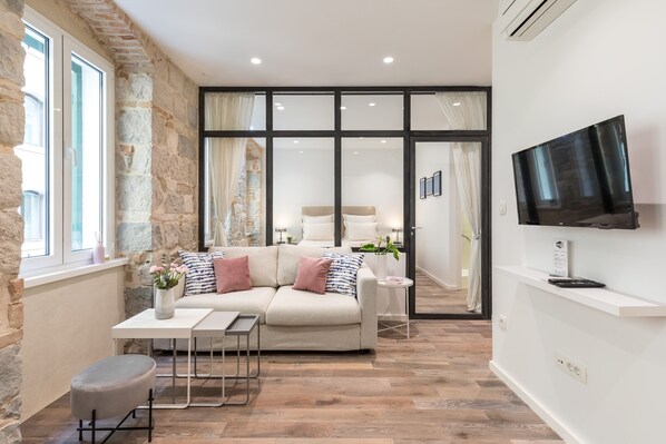 A modern living room with a sofa, coffee table, and ottoman, a flat-screen TV mounted on the wall, and a stone wall.