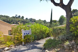 A sign for 'Acces Plage' with a gravel path leading to a building, surrounded by greenery and trees.