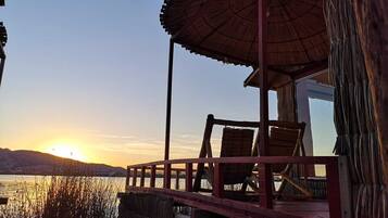 Une terrasse en bois, avec des chaises et un parasol, donnant sur une étendue d’eau au coucher du soleil.