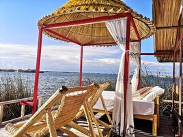 A thatched gazebo with a white canopy and red frame, overlooking a body of water.