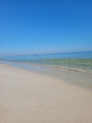 Een strand met helderblauw water, een zandstrand en een pier die in zee reikt.