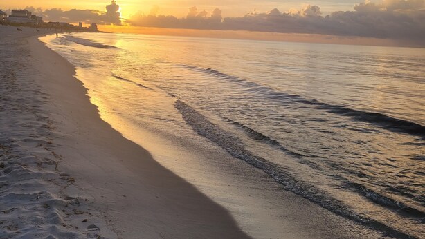 Una playa con un mar tranquilo, cielo despejado y una puesta de sol.