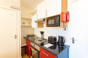 Compact kitchen with a modern design, featuring a black countertop, stainless steel appliances, a sink, and a compact oven.