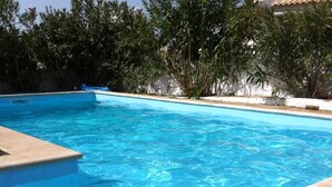 A rectangular swimming pool with clear blue water, surrounded by a concrete edge and a tiled deck.