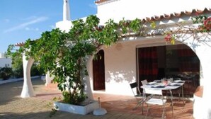 A patio area with a table and chairs, a white building with a tiled roof, and a potted plant.