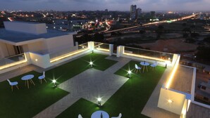 A rooftop terrace with outdoor seating and a city view at dusk.