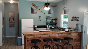 Une cuisine avec un îlot central en bois, des tabourets de bar, un ventilateur de plafond et un réfrigérateur.