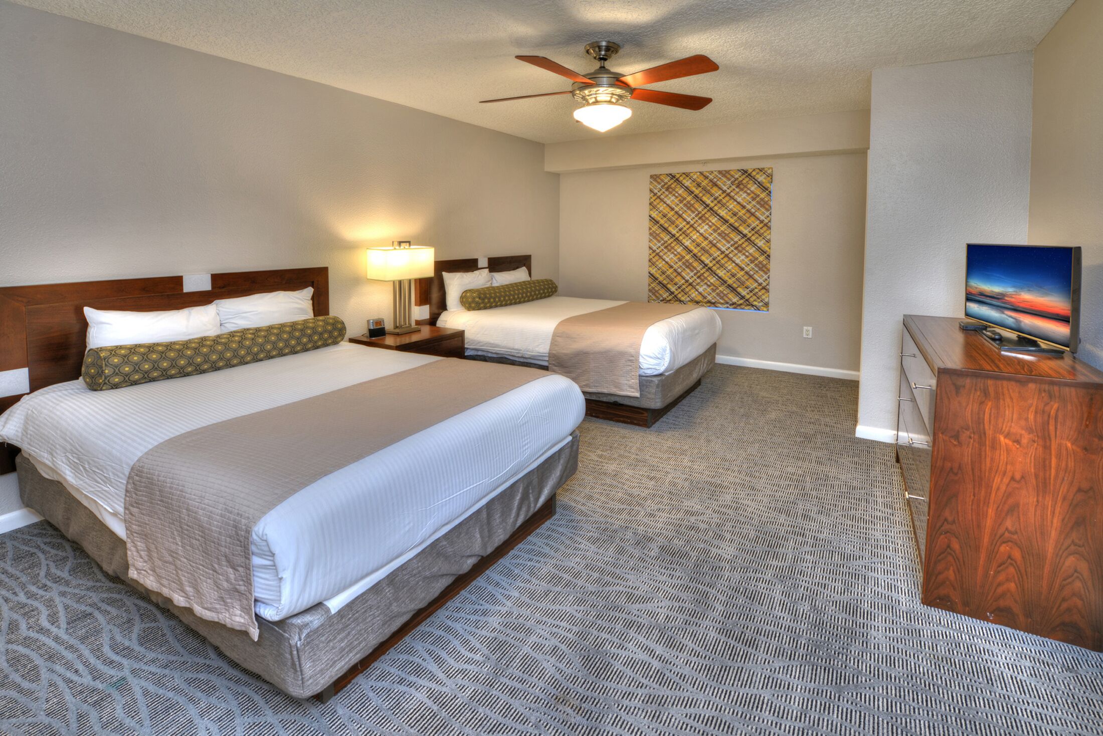 A hotel room with two beds, a ceiling fan, a TV, and a patterned carpet.