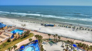 A beach resort with a swimming pool, beach umbrellas, and a lifeguard tower.