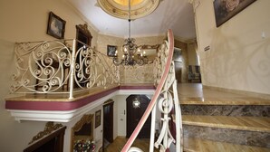 Un magnifique escalier orné de rampes en métal ouvragé et surmonté d’un lustre, menant à une pièce dotée d’un plancher en bois et d’un grand miroir.