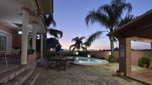 Une terrasse en pierre avec une piscine, du mobilier d’extérieur et des palmiers.