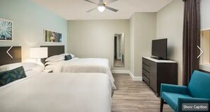 Two single beds with white linens and matching headboards, a flat-screen TV, and a seating area with a chair and dresser.