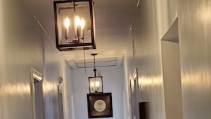 A hallway with a wooden floor, white walls, and a hanging light fixture. There are two framed pictures on the wall. - Ida's Oasis  near JRMC Hospital ,  Pine Bluff Country Club & Restaurants . (Pine Bluff)