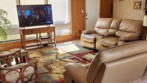 A living room with a television, leather sofa, wooden chair, and a patterned rug. - Ida's Oasis  near JRMC Hospital ,  Pine Bluff Country Club & Restaurants . (Pine Bluff)